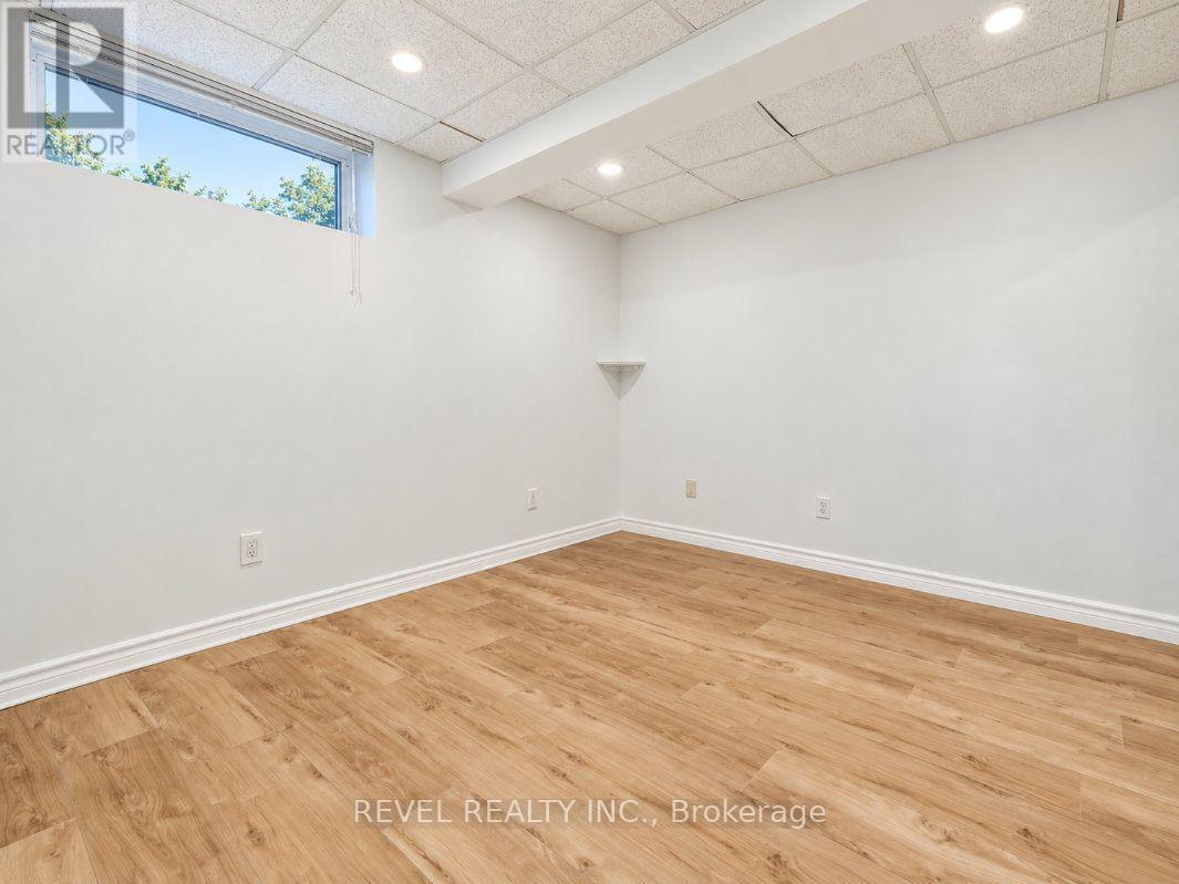 Empty room with wood-look flooring, a high horizontal window, and a suspended tile ceiling.