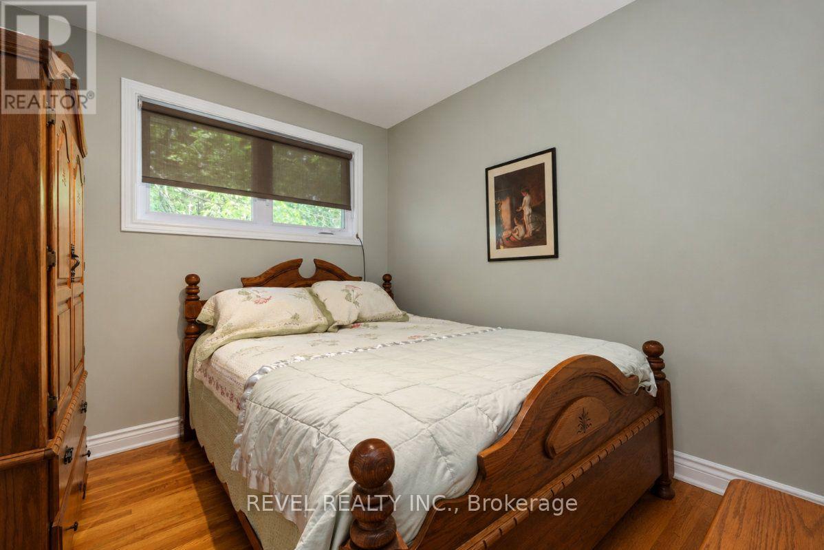 Furnished bedroom with a carved wooden bed, matching wardrobe, hardwood floors and a wide shaded window.