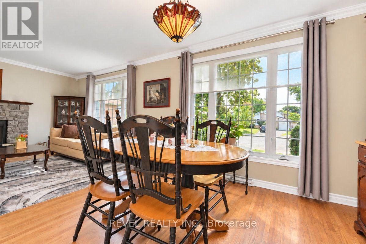 Dining room with a wooden table, dark chairs, tall curtained windows, and a colorful pendant light.