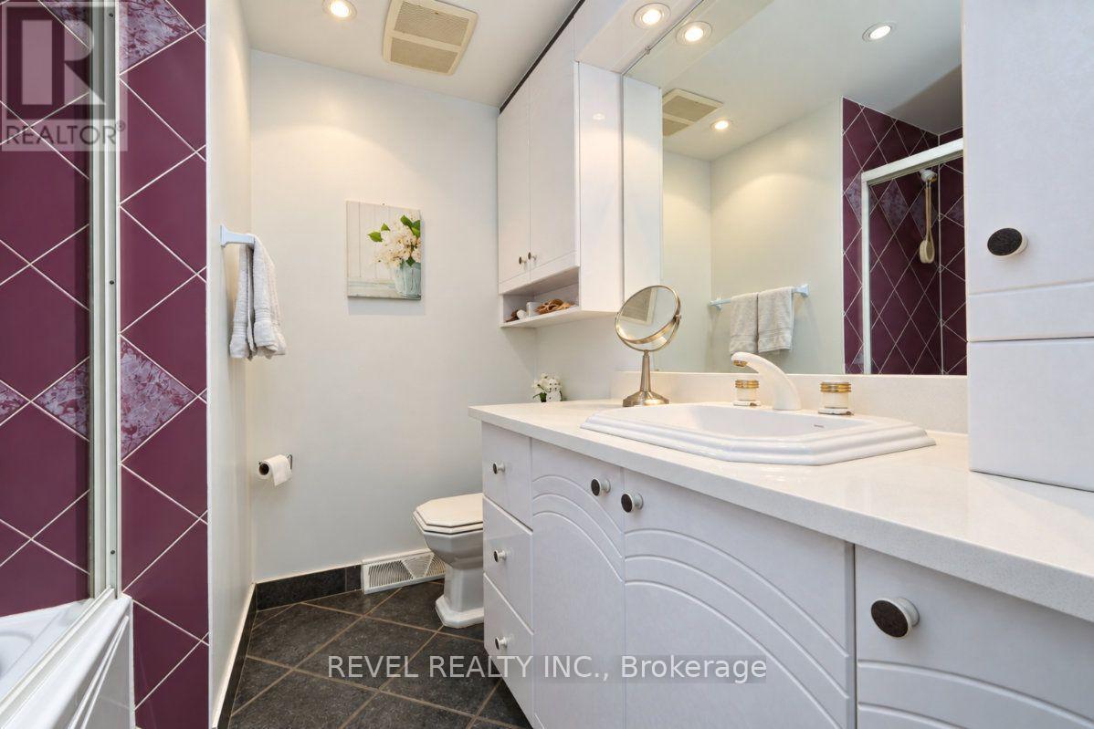Bathroom with a white vanity, large mirror, and burgundy-tiled shower.