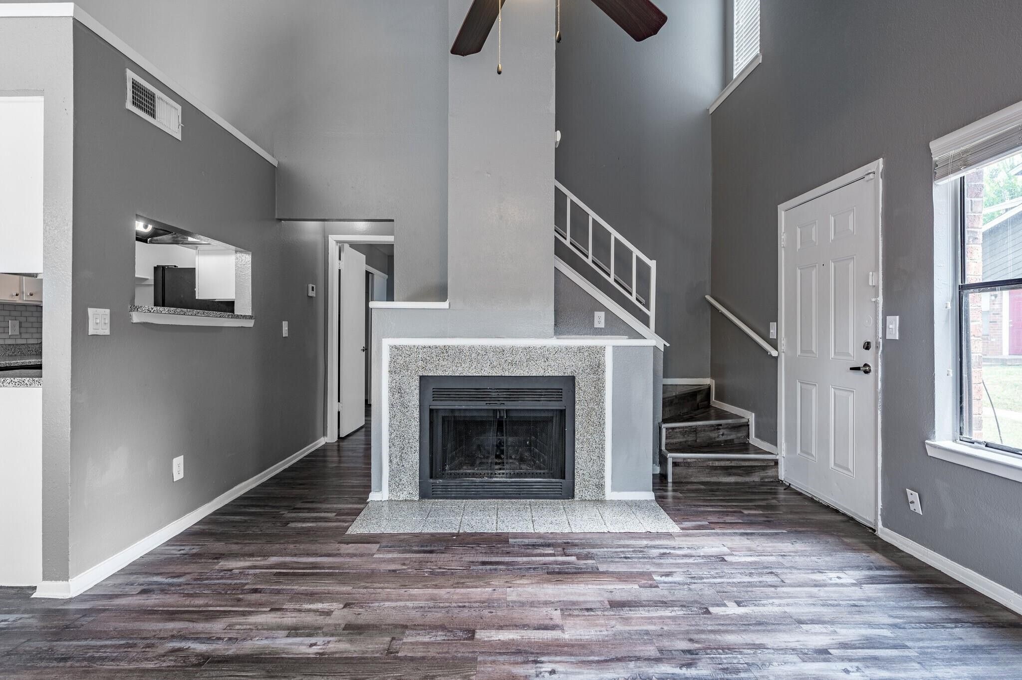 Unfurnished living room with a fireplace, staircase, and dark wood-look floors.