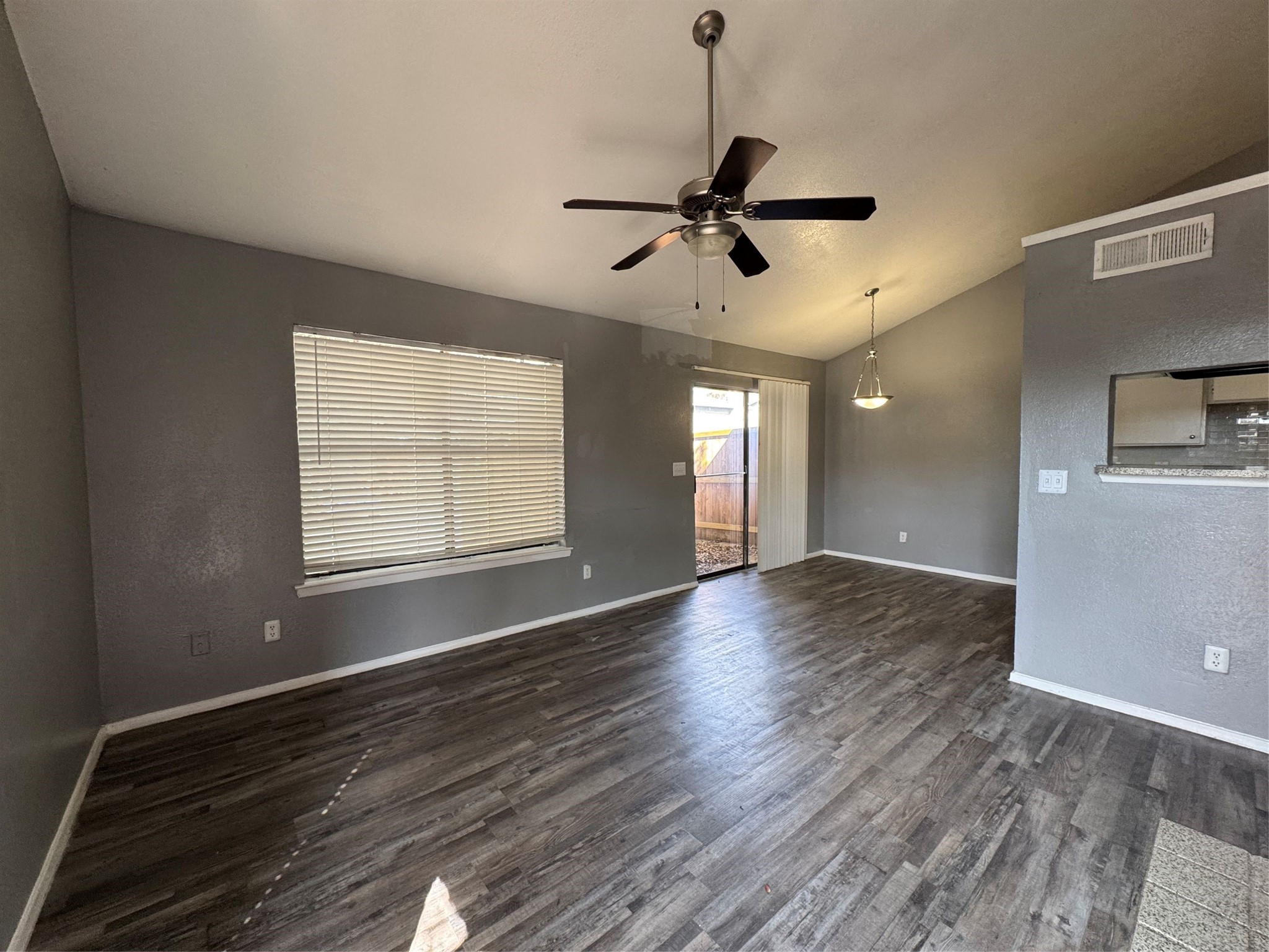Vacant living and dining area with dark wood-look flooring, ceiling fan, and sliding glass door.