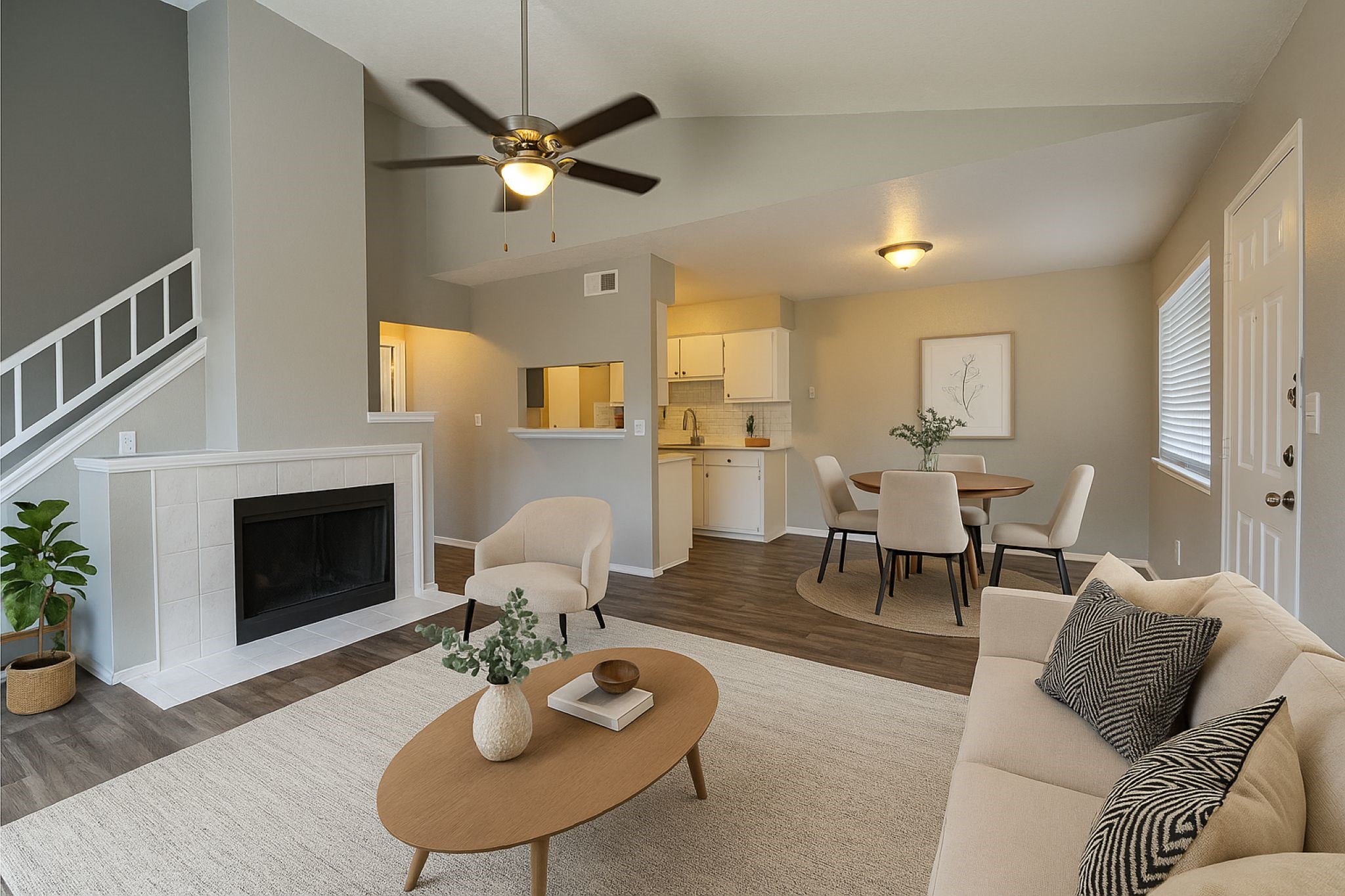 Open-plan living room with a white-tiled fireplace, cream furnishings, and dining area beside the kitchen.