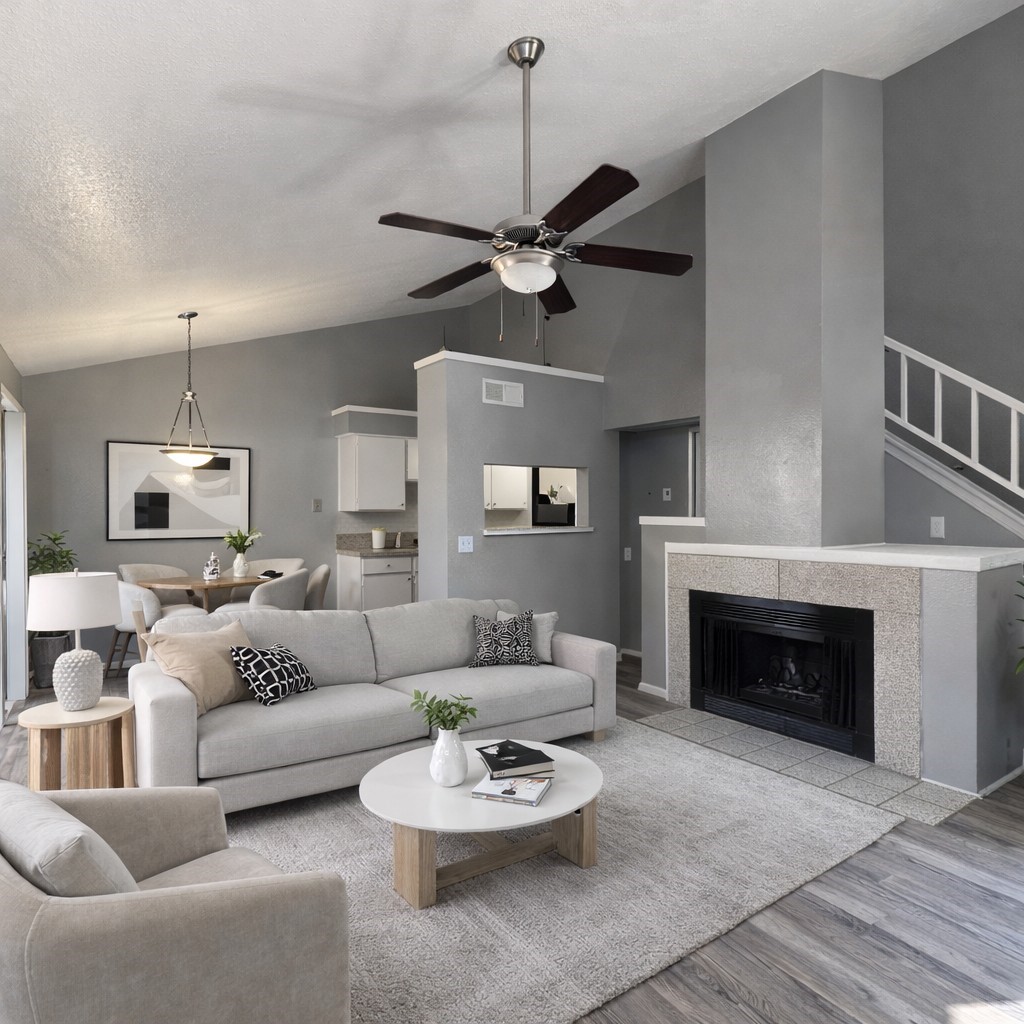 Living room with gray sofas, a tiled fireplace, and a dark ceiling fan beneath a vaulted ceiling.