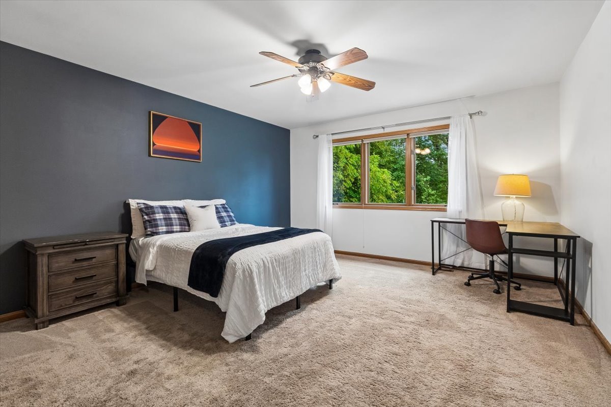 Bedroom with a bed against a dark blue accent wall and a desk beside a tree-lined window.
