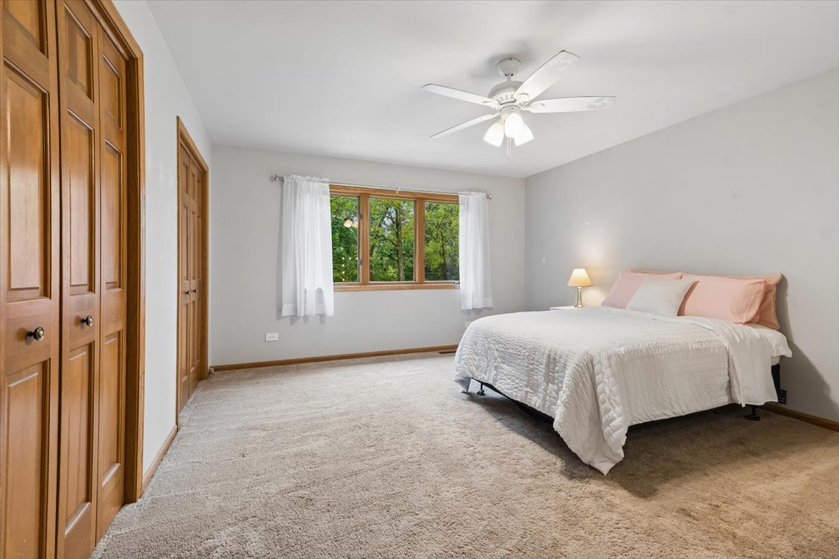 Bedroom with a white bed, wooden closet doors, and a window overlooking trees.