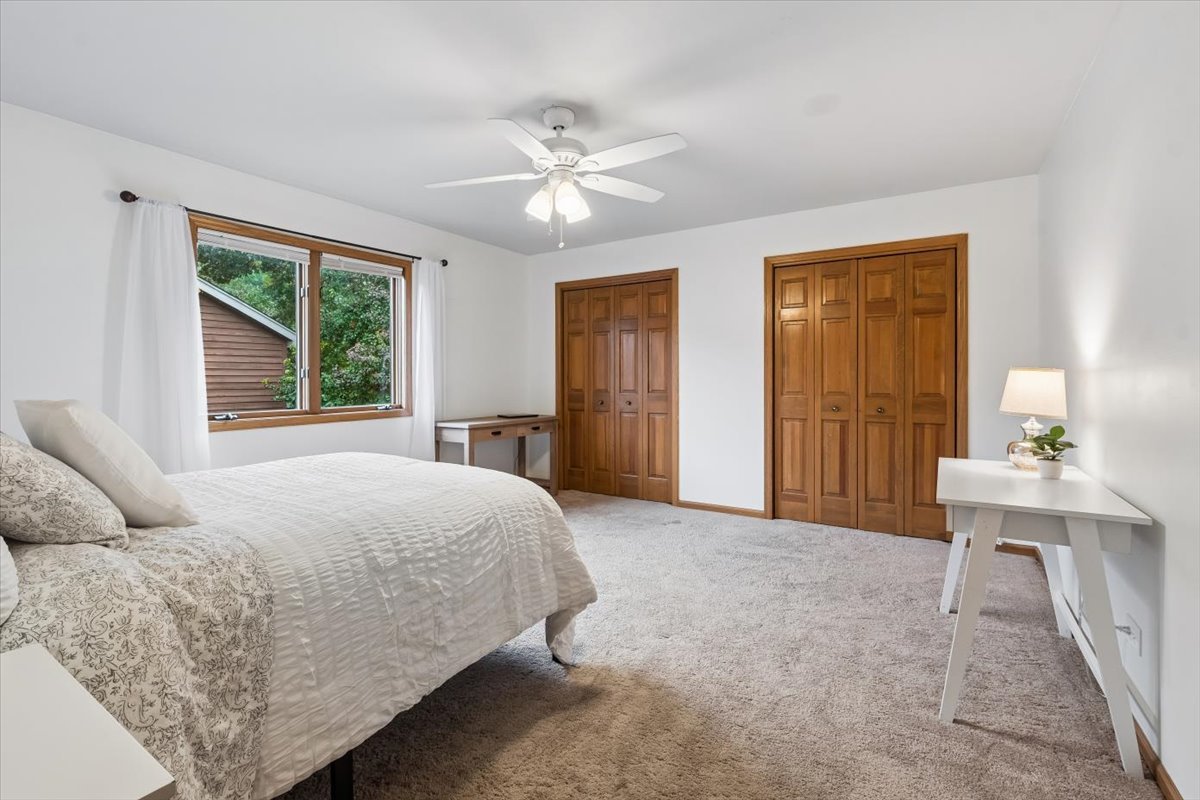 Bedroom with white bedding, two wooden closets, and a ceiling fan.
