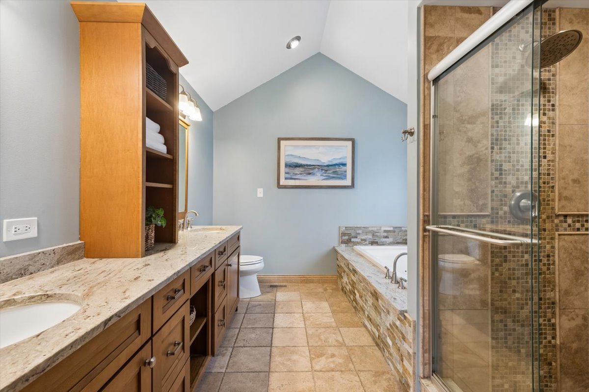 Bathroom with a long wood vanity, built-in soaking tub, and glass-enclosed tiled shower.