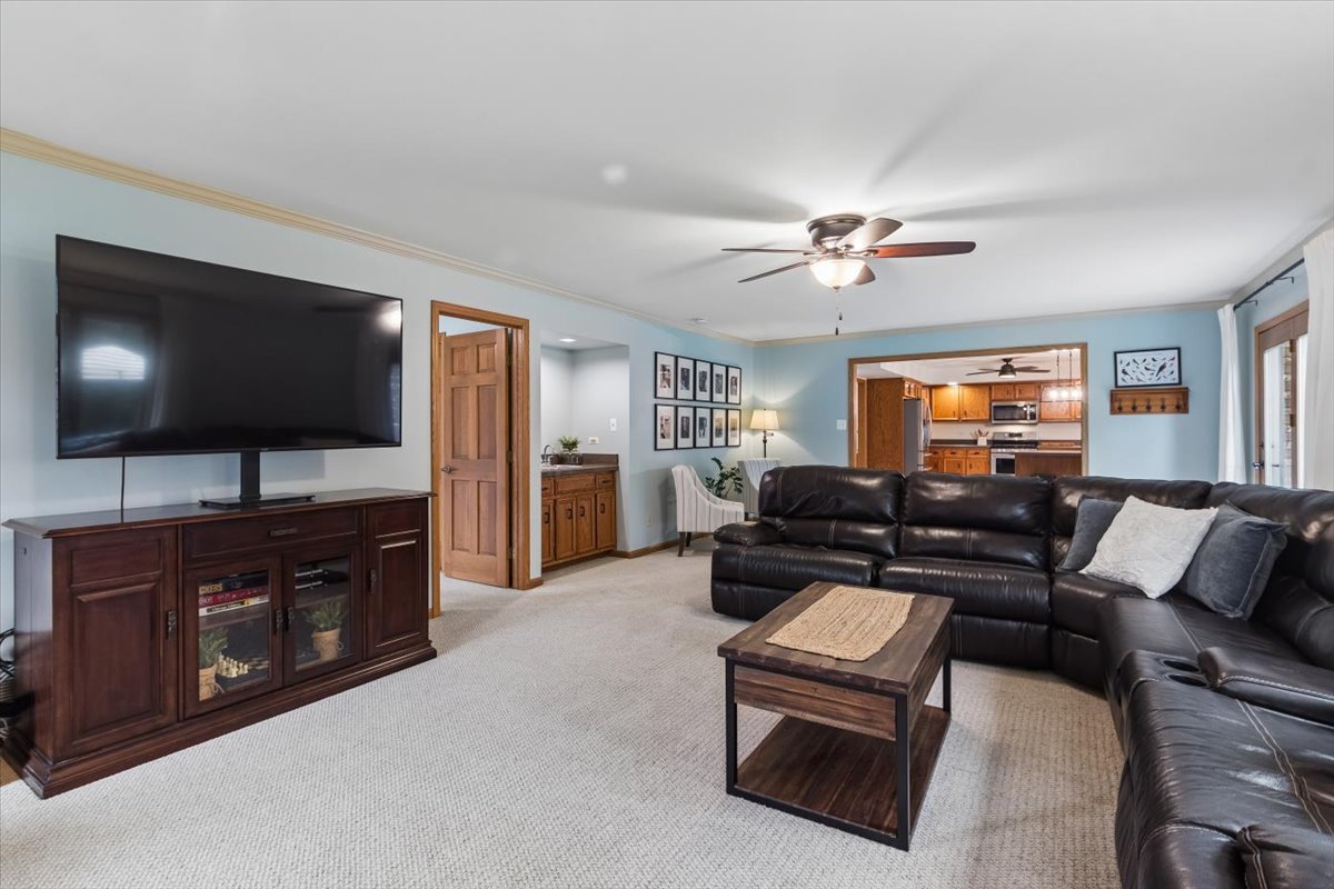Living room with a dark leather sectional, large television, and view into a wood-cabinet kitchen.