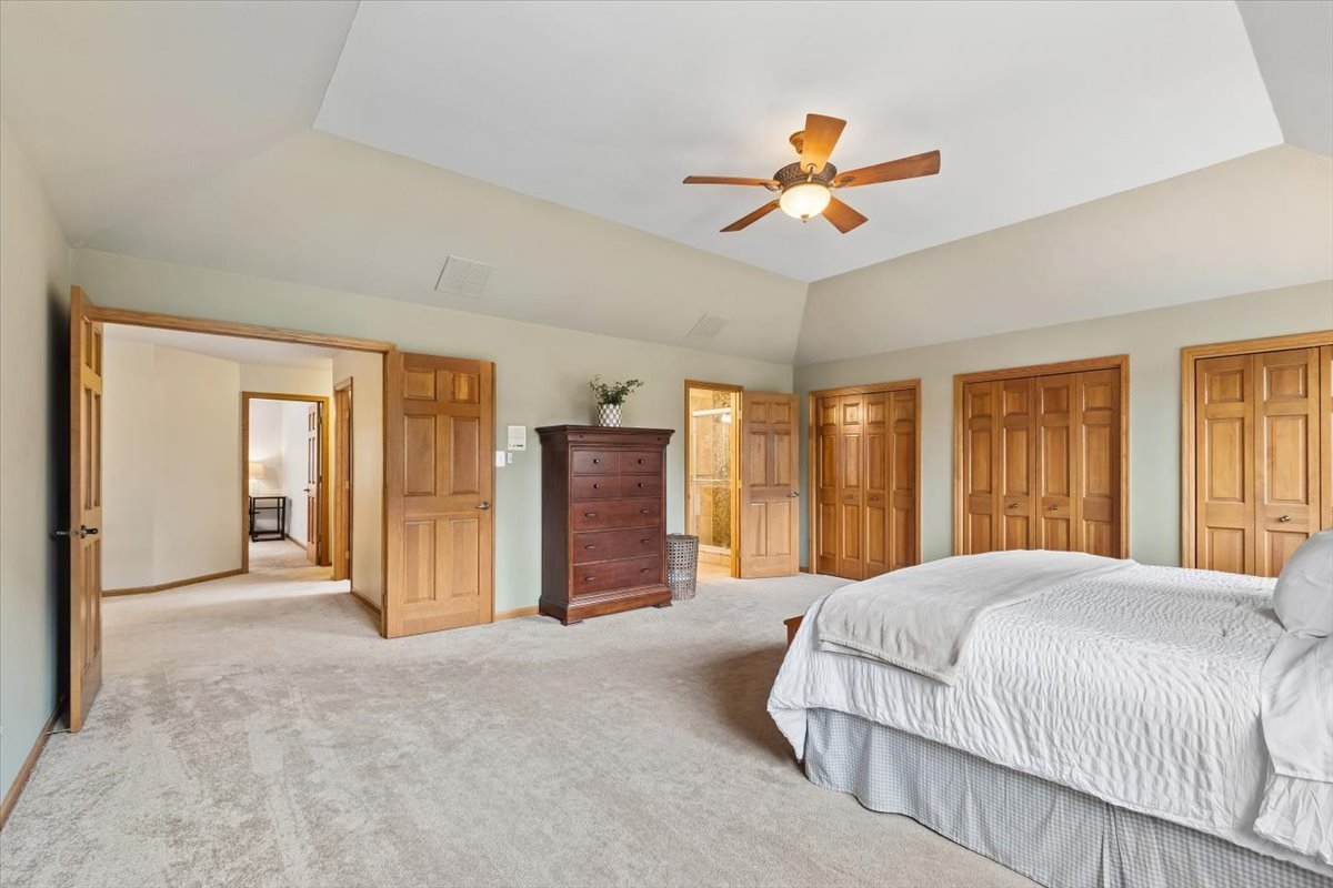 Spacious bedroom with vaulted ceiling, wood-blade ceiling fan, and multiple paneled wood doors.