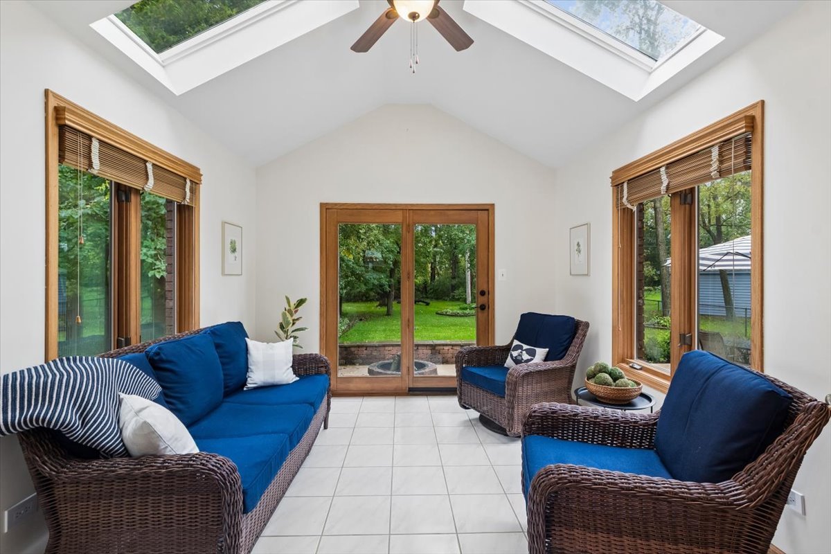 Sunroom with blue-cushioned wicker seating, skylights, and glass doors overlooking a green backyard.