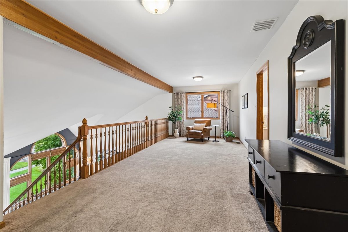 Carpeted loft landing with a wooden railing overlooking the entryway and a chair beside the window.