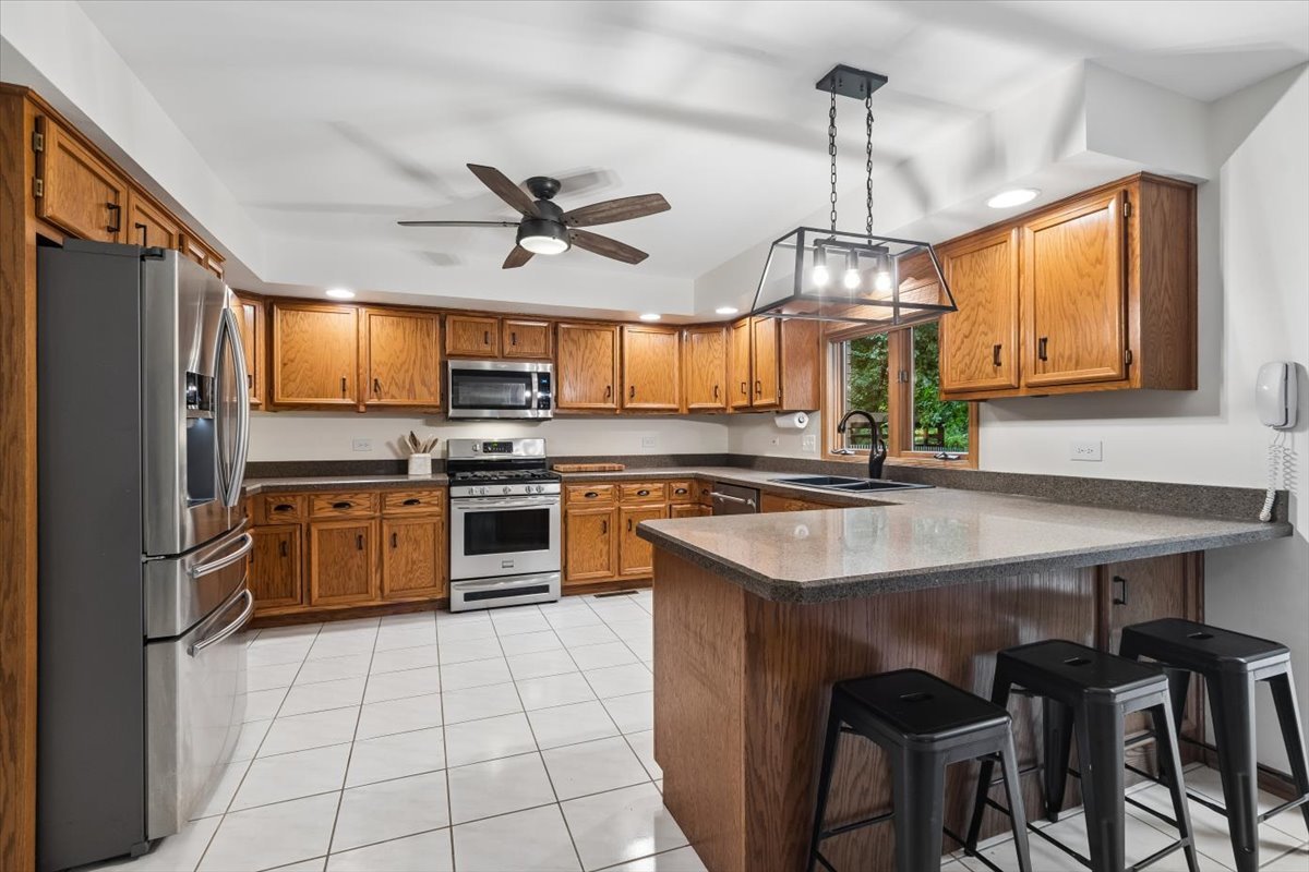 Kitchen with oak cabinetry, stainless steel appliances, and a large island with three bar stools.