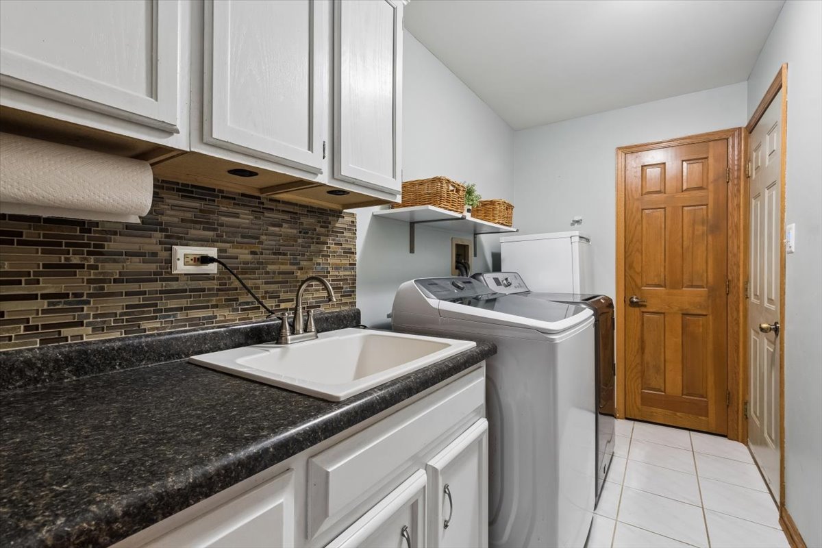 Laundry room with a utility sink, front-loading washer and dryer, and dark tile backsplash.