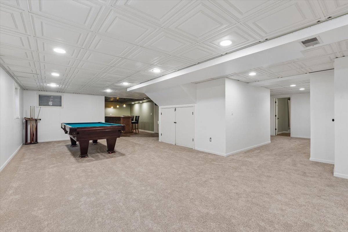 Finished basement game room with a pool table, cue rack, and small bar area.