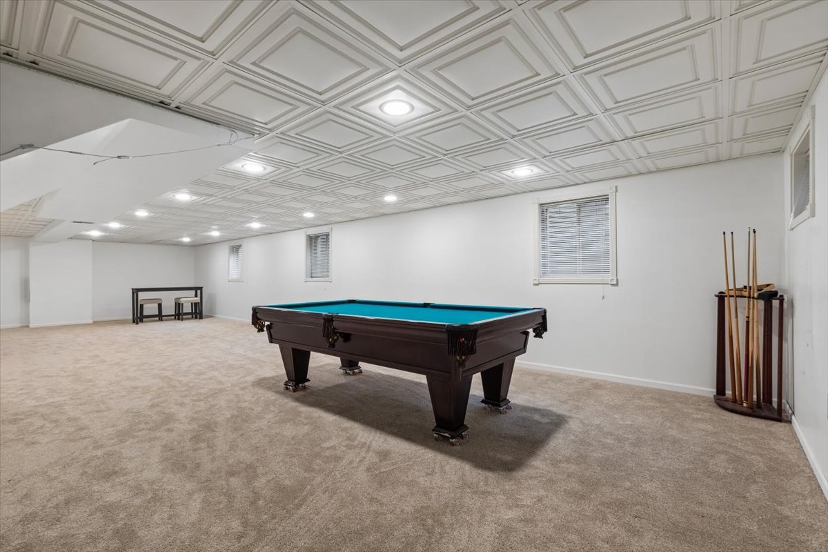 Basement game room with a billiards table, cue rack, and ornate geometric ceiling.