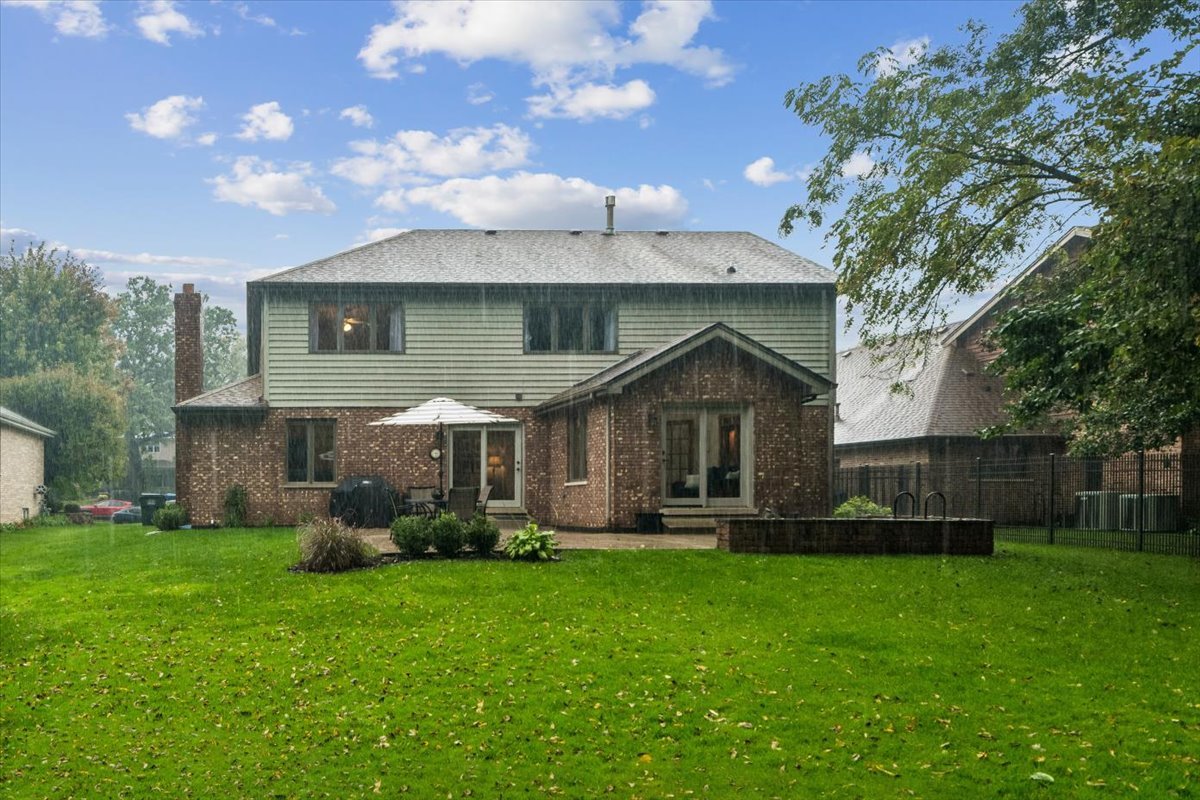 Home’s brick-and-siding rear exterior overlooks a broad lawn, patio, and fenced pool area.