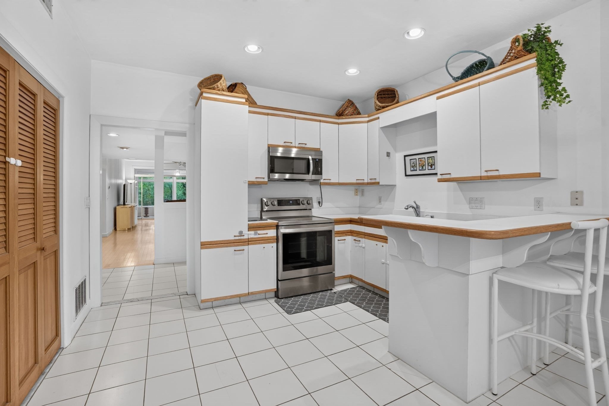 Kitchen with white cabinets, wood trim, stainless appliances, tiled floor, and a peninsula with bar stools.