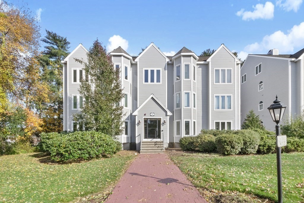 Gray-sided residential building with bay windows and a brick walkway leading to its central entrance.