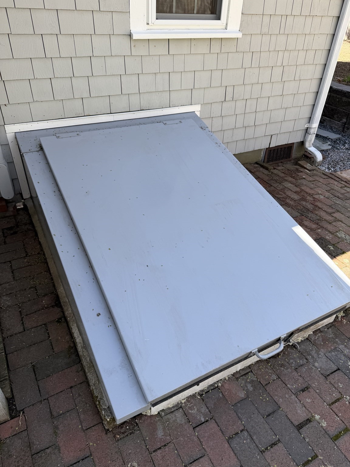 White basement bulkhead hatch beside the house on a brick patio.