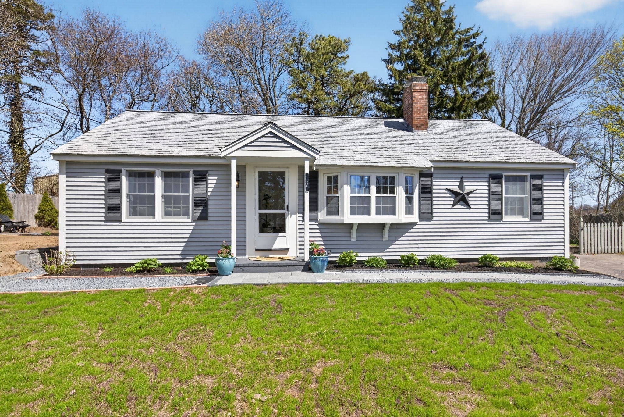 Gray single-story house with white trim, black shutters, a bay window, and a black star on the facade.