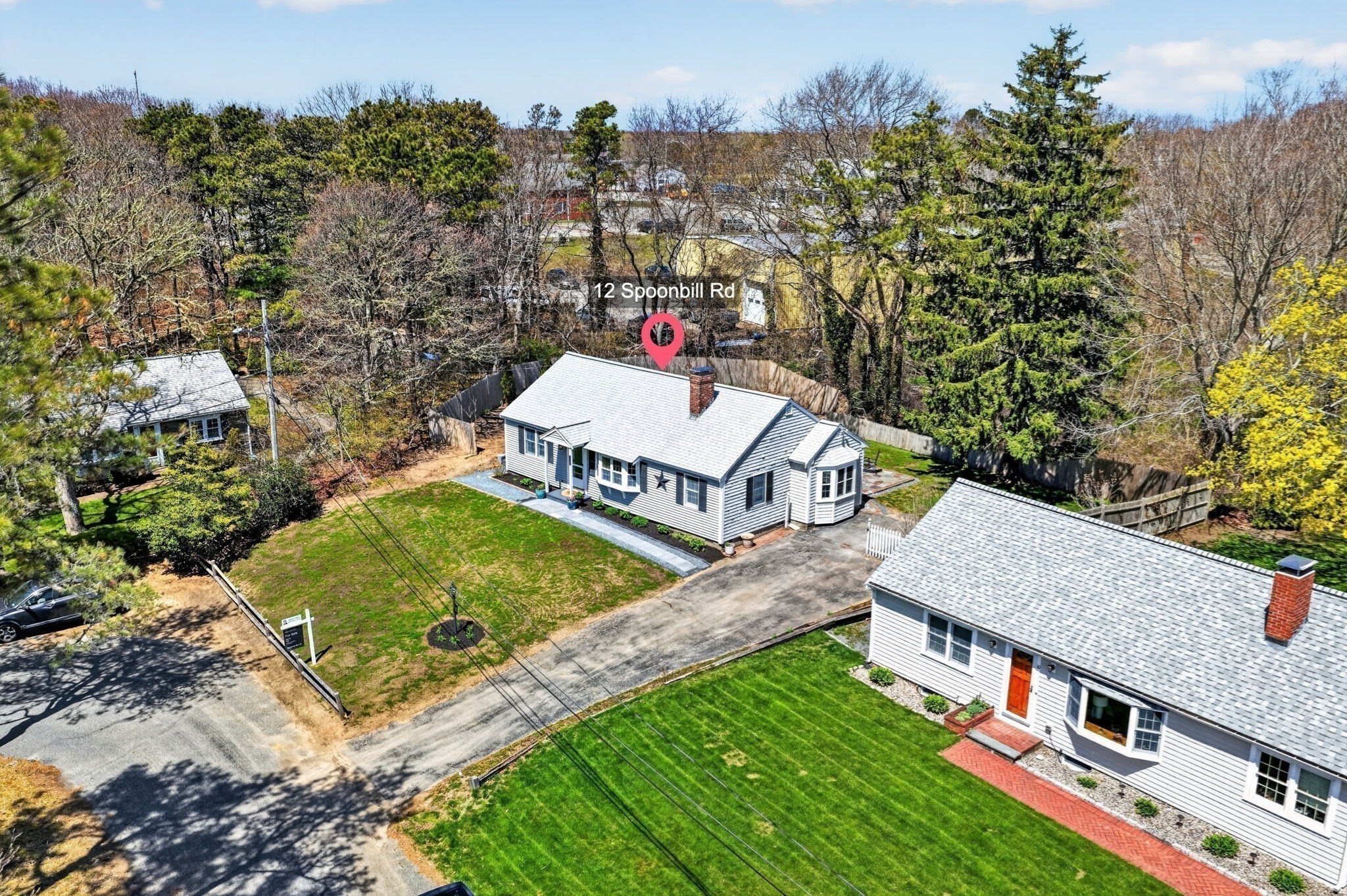 Aerial view of 12 Spoonbill Rd, a gray-sided home with a fenced lawn and driveway.