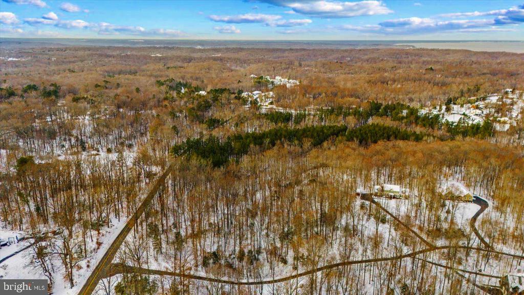 Aerial view of snow-dusted woodland, winding roads, scattered homes, and distant water.