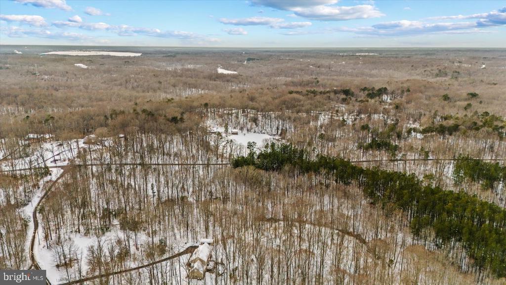Snow-dusted wooded lot with a small building, access road, and distant waterway.