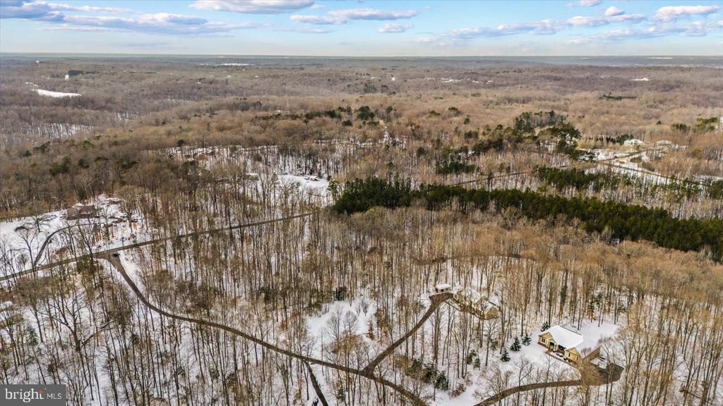 Aerial view of a wooded, snow-covered lot with winding roads and scattered homes.