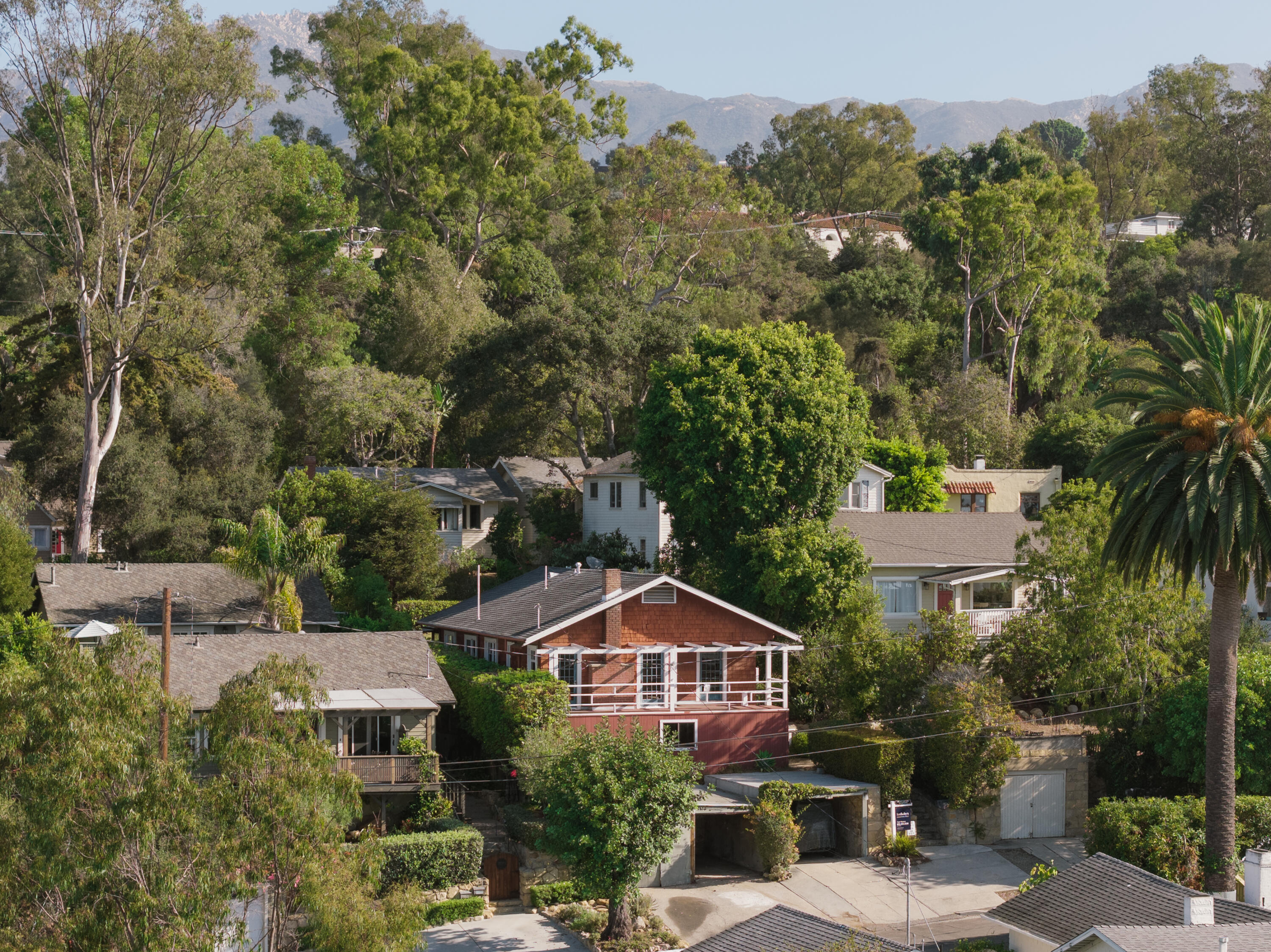 Hillside homes among mature trees, with a red-shingle house and mountain foothills behind.