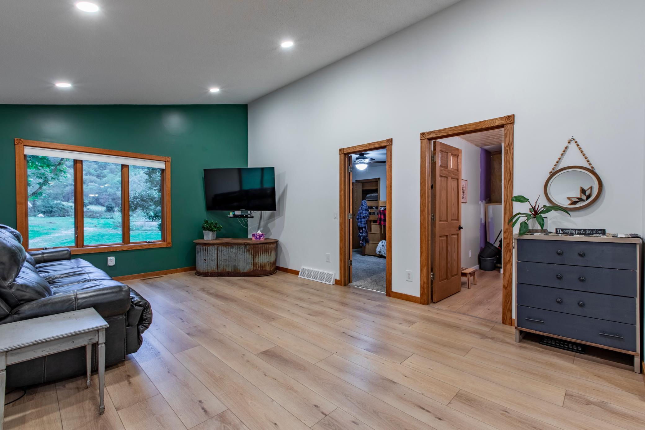 Living room with a green accent wall, leather sectional, and large window overlooking the lawn.