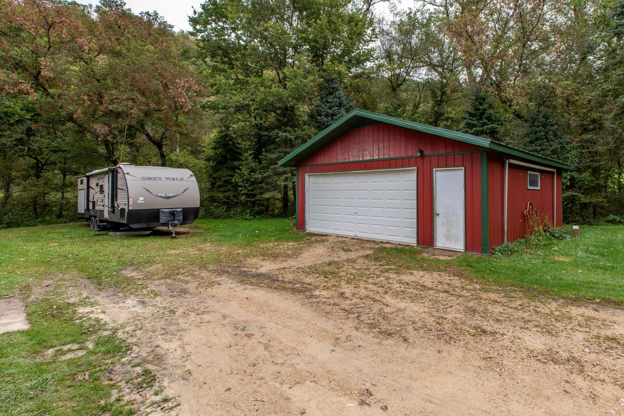 Red detached garage beside a travel trailer, surrounded by autumn trees.