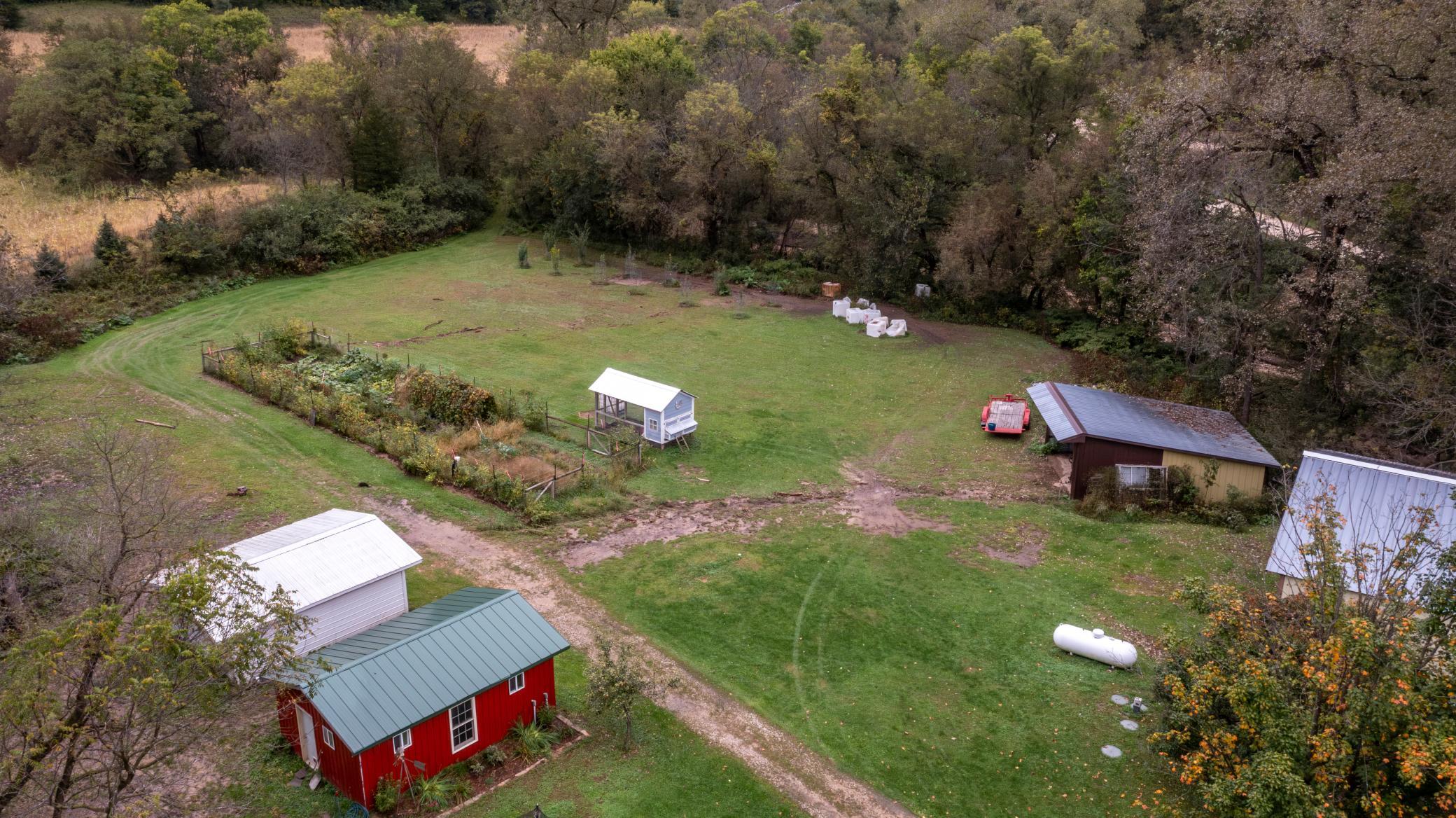 Aerial view of a rural yard with a fenced garden, red shed, and surrounding woods.