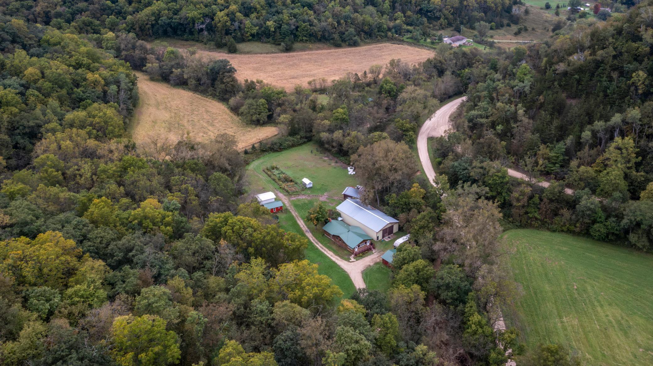 Aerial view of a rural property with farm buildings, open fields, and surrounding woods.