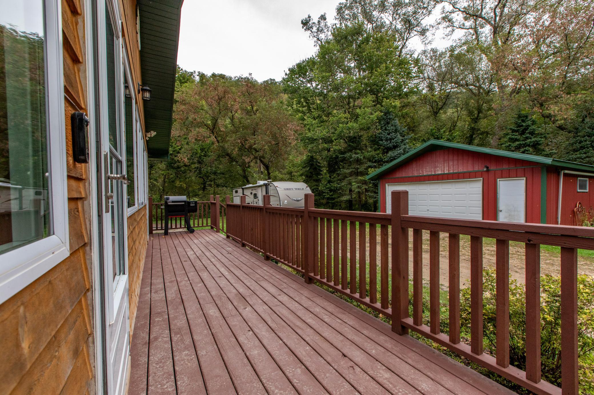 Wooden deck beside a house, overlooking a red garage and wooded yard.