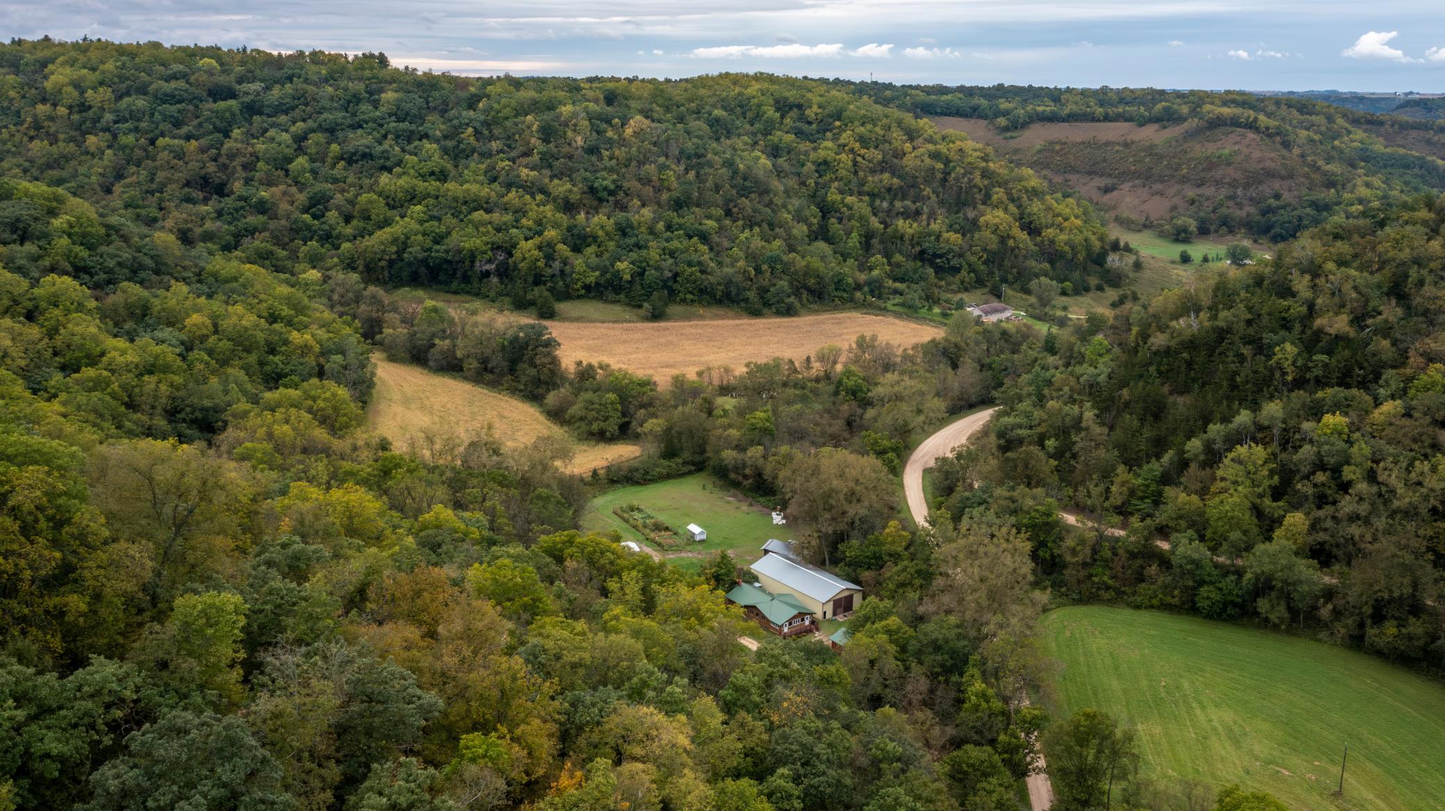 Aerial view of a rural property amid wooded hills, open fields, and a winding gravel road.