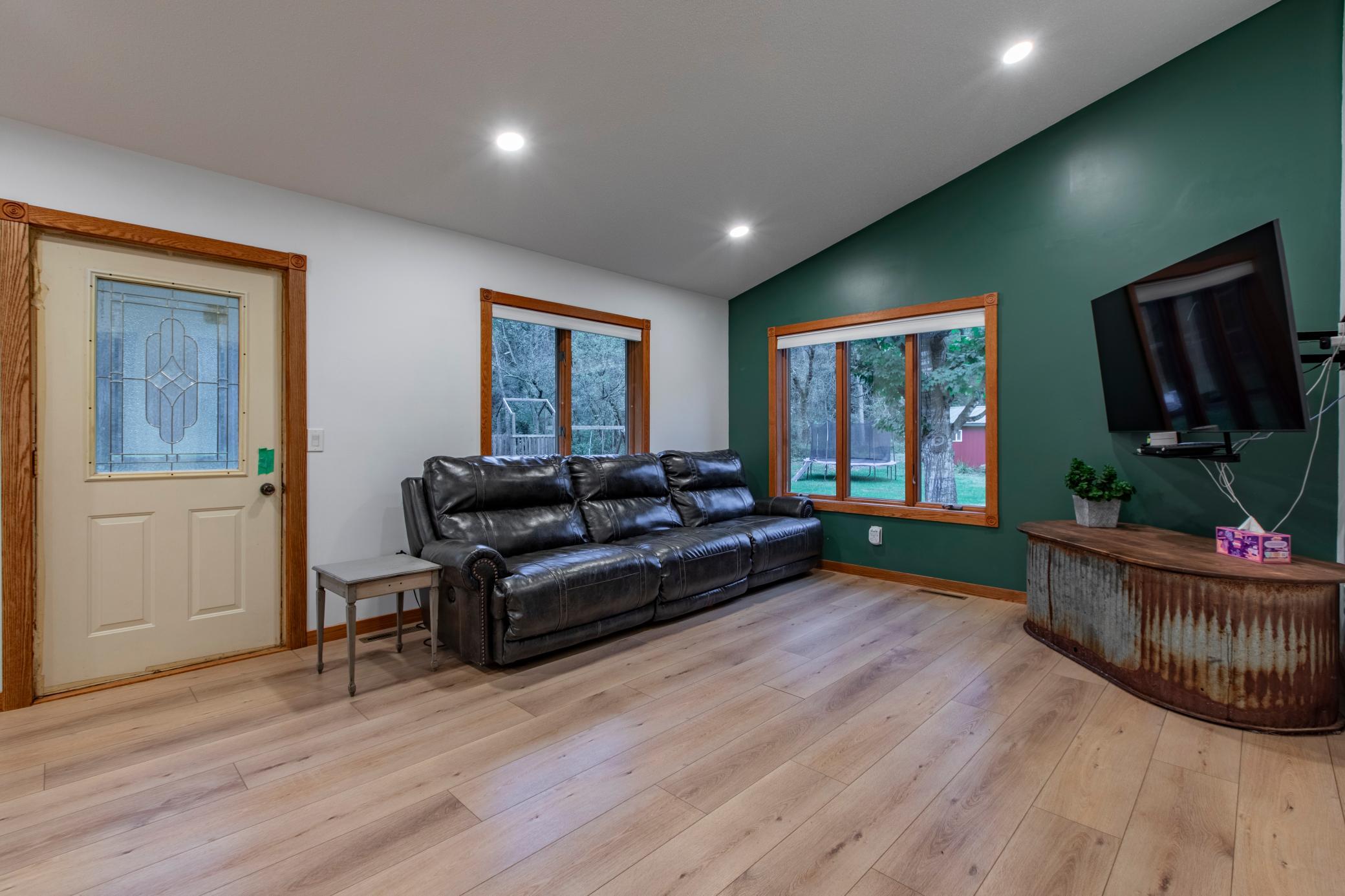 Living room with a black leather sofa, green accent wall, large windows, and wall-mounted television.
