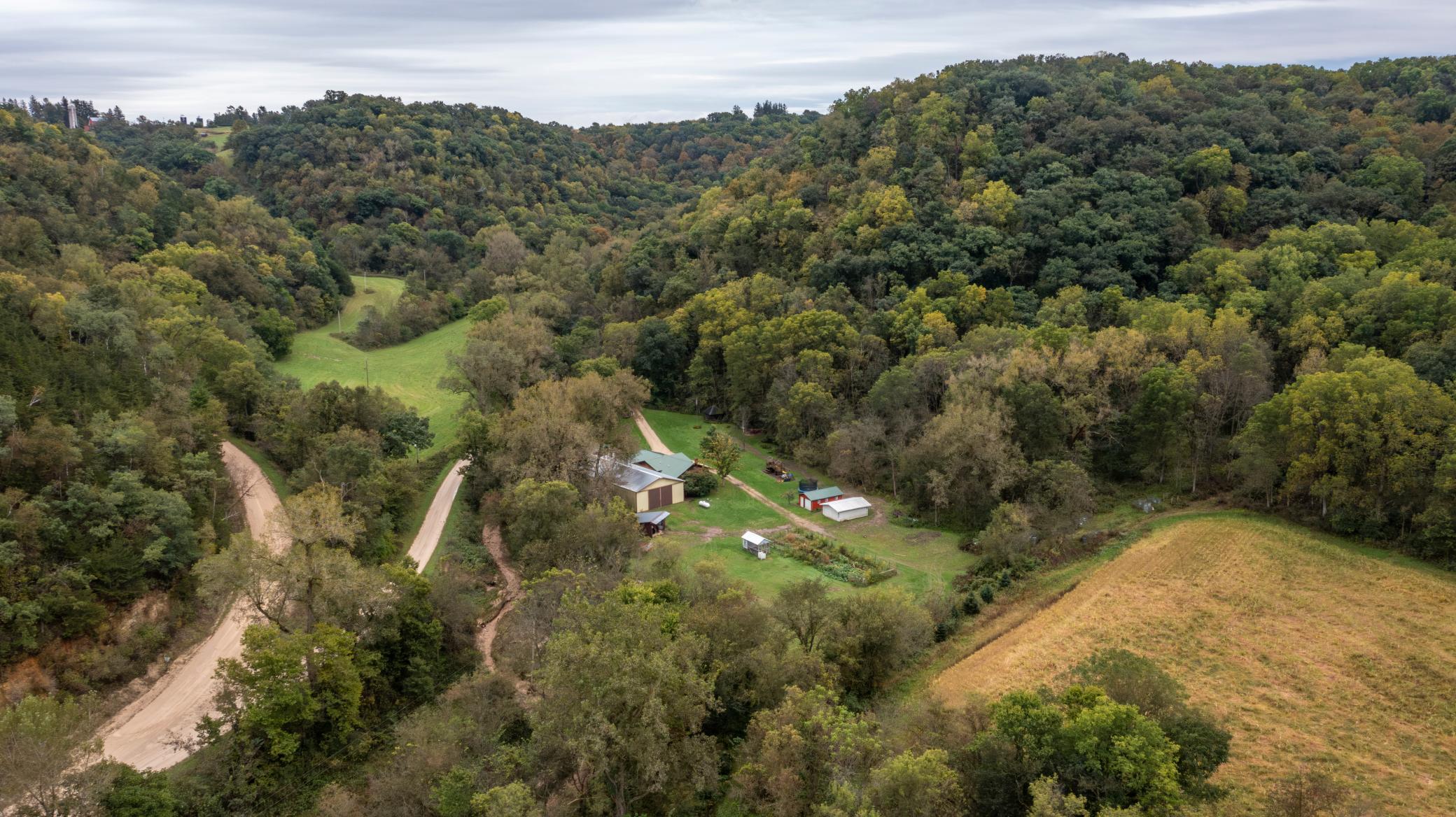 Aerial view of a wooded rural property with outbuildings, open fields, and winding gravel roads.