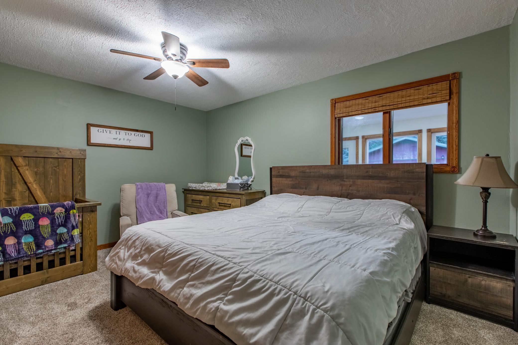 Bedroom with a dark wood bed, white quilt, sage green walls, and a wooden crib.