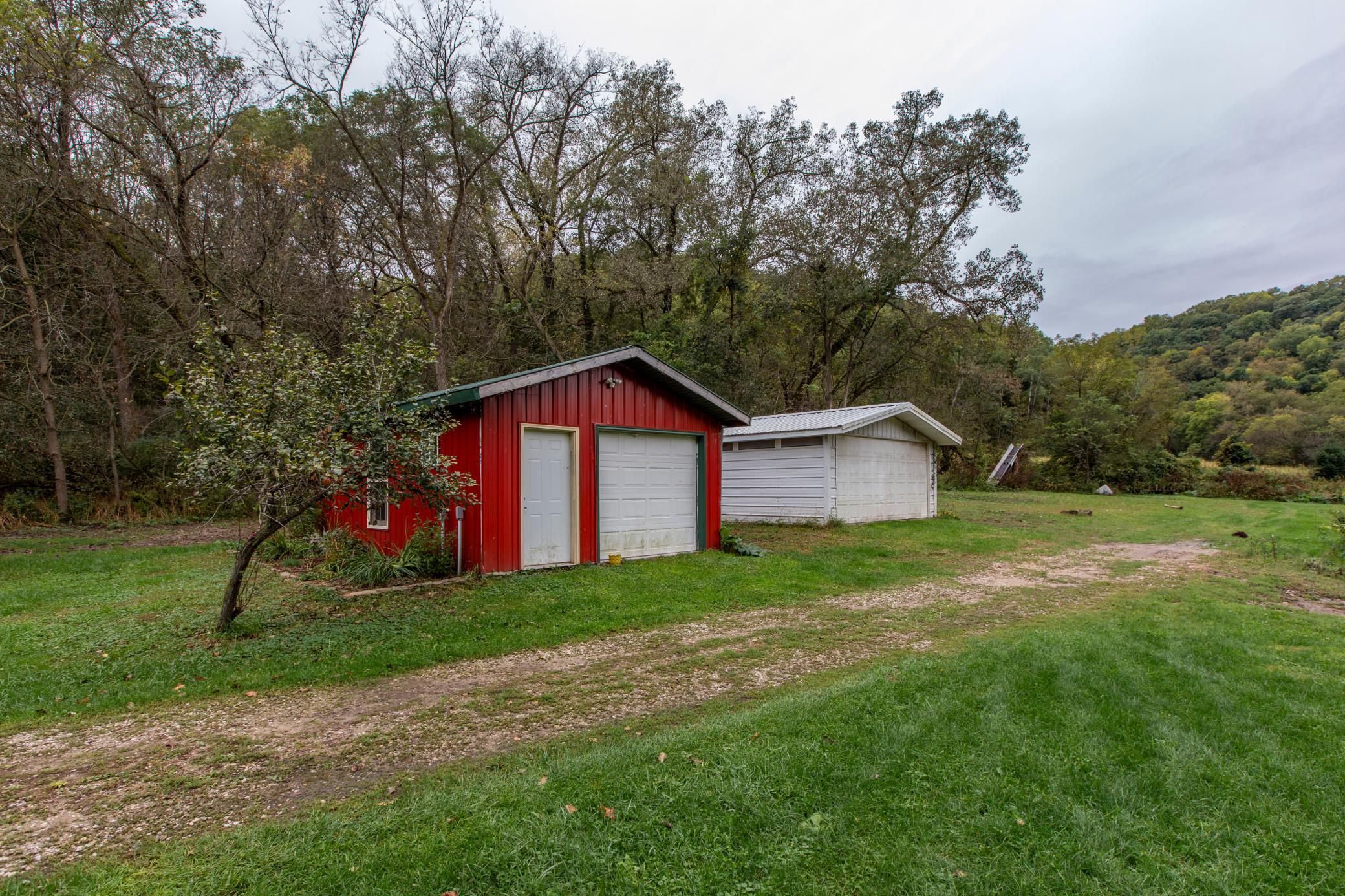 Red and white detached garages beside a gravel drive, surrounded by wooded hills.