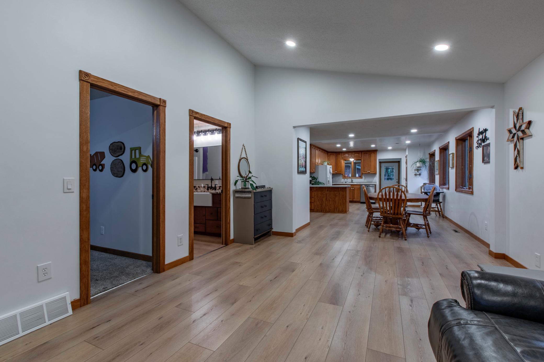 Open living and dining area leading to a kitchen, with wood-look floors and warm wood trim.