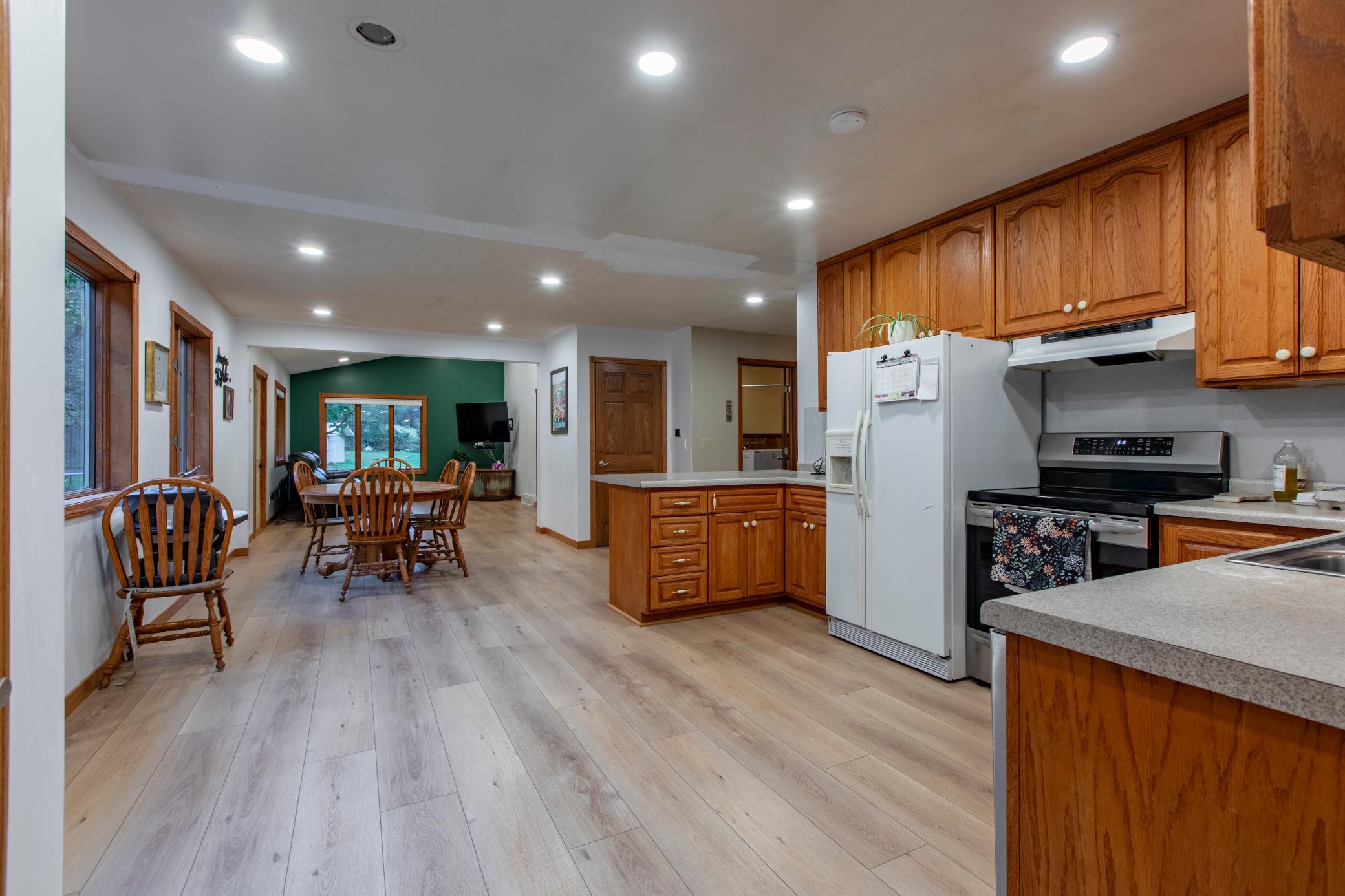 Open kitchen and dining area with warm wood cabinetry, a central island, and a green accent wall.