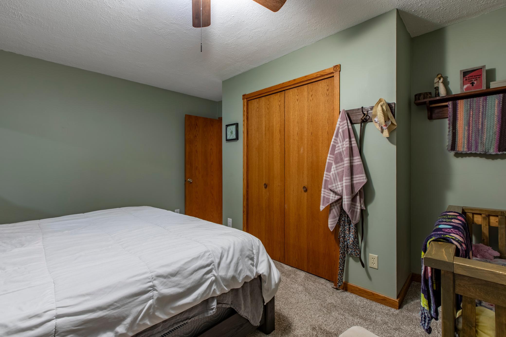 Bedroom with a white-covered bed, sage-green walls, and wooden closet doors.