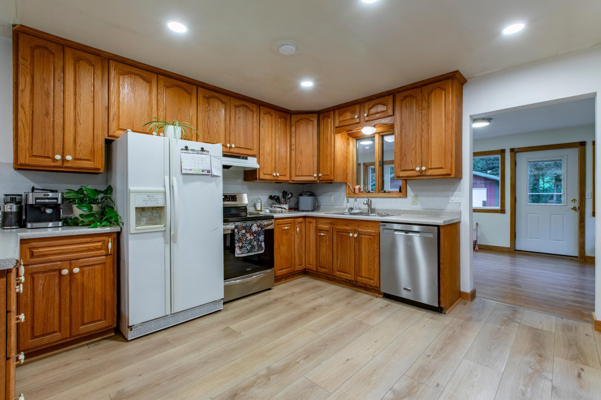 Kitchen with honey-colored wood cabinets, light flooring, and white and stainless steel appliances.