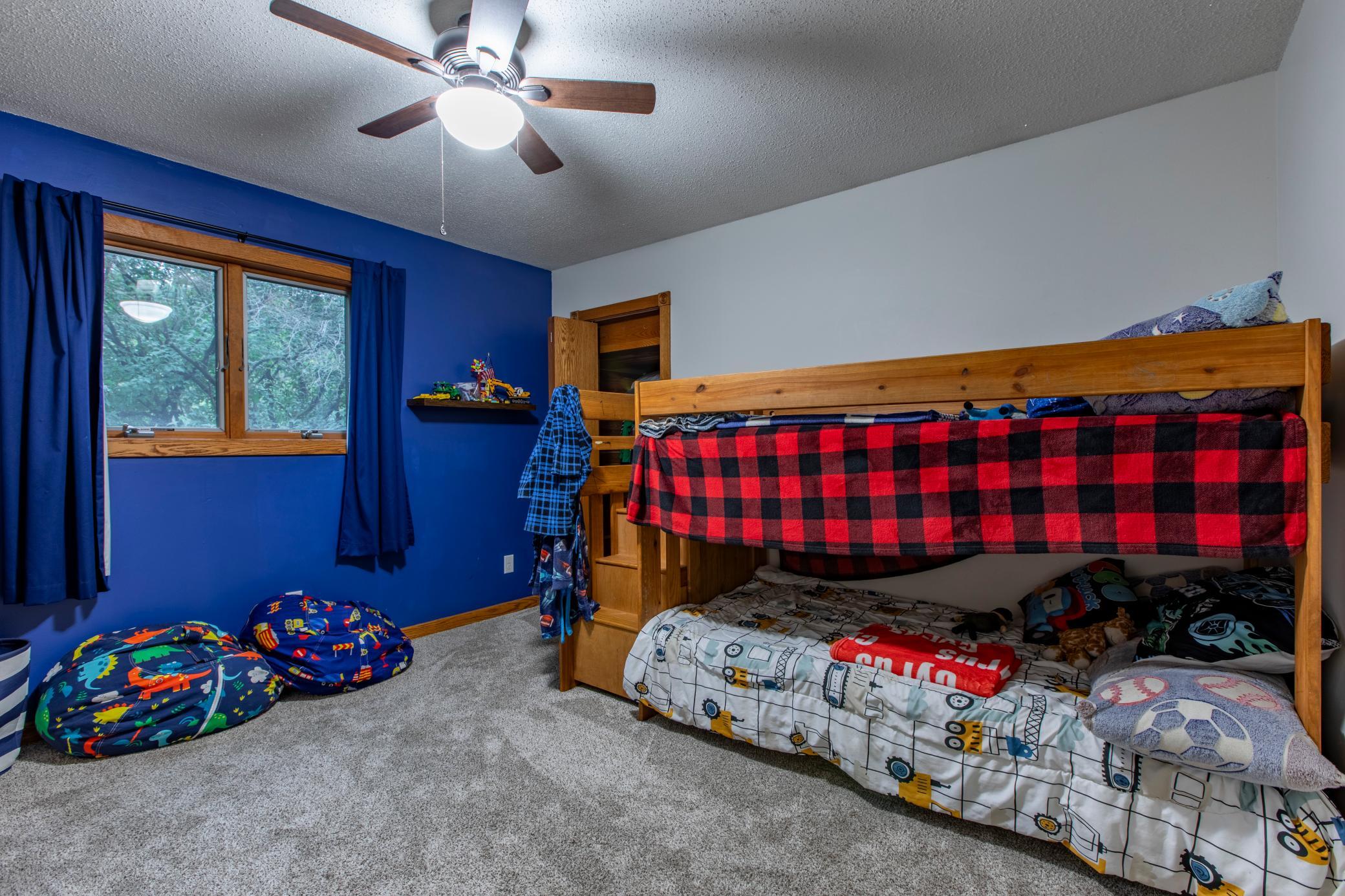 Bedroom with a wooden bunk bed, red plaid blanket, blue walls, and a wood-trimmed window.