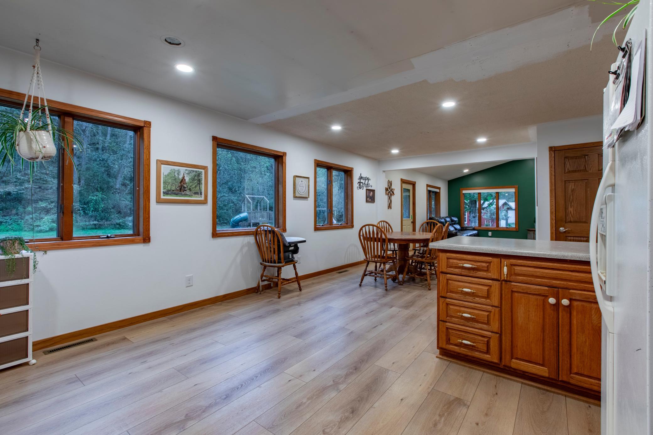 Kitchen and dining area with warm wood cabinetry, large windows, and a green accent wall.