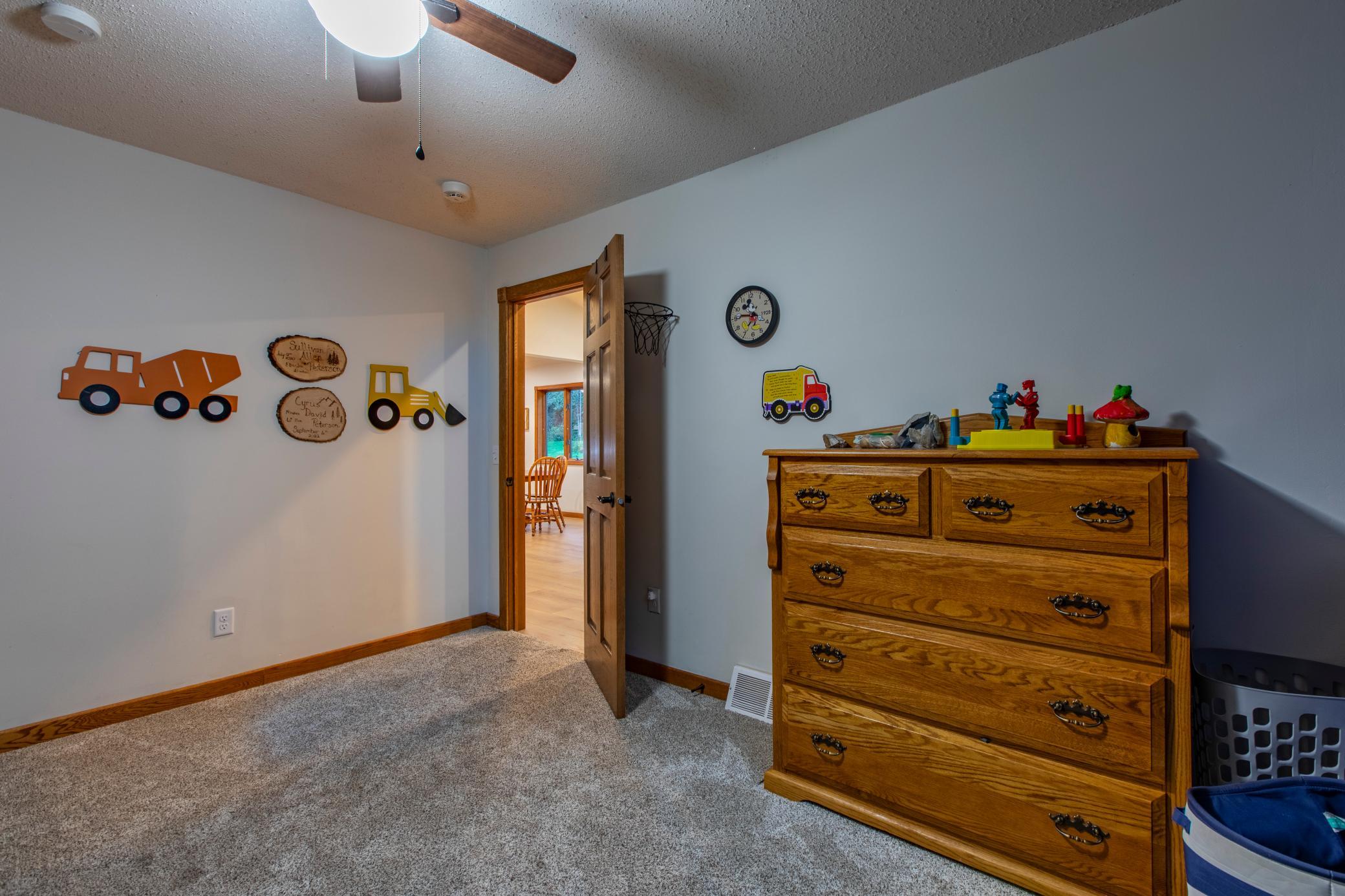 Bedroom with gray carpet, construction vehicle wall decorations, and a large wooden dresser.