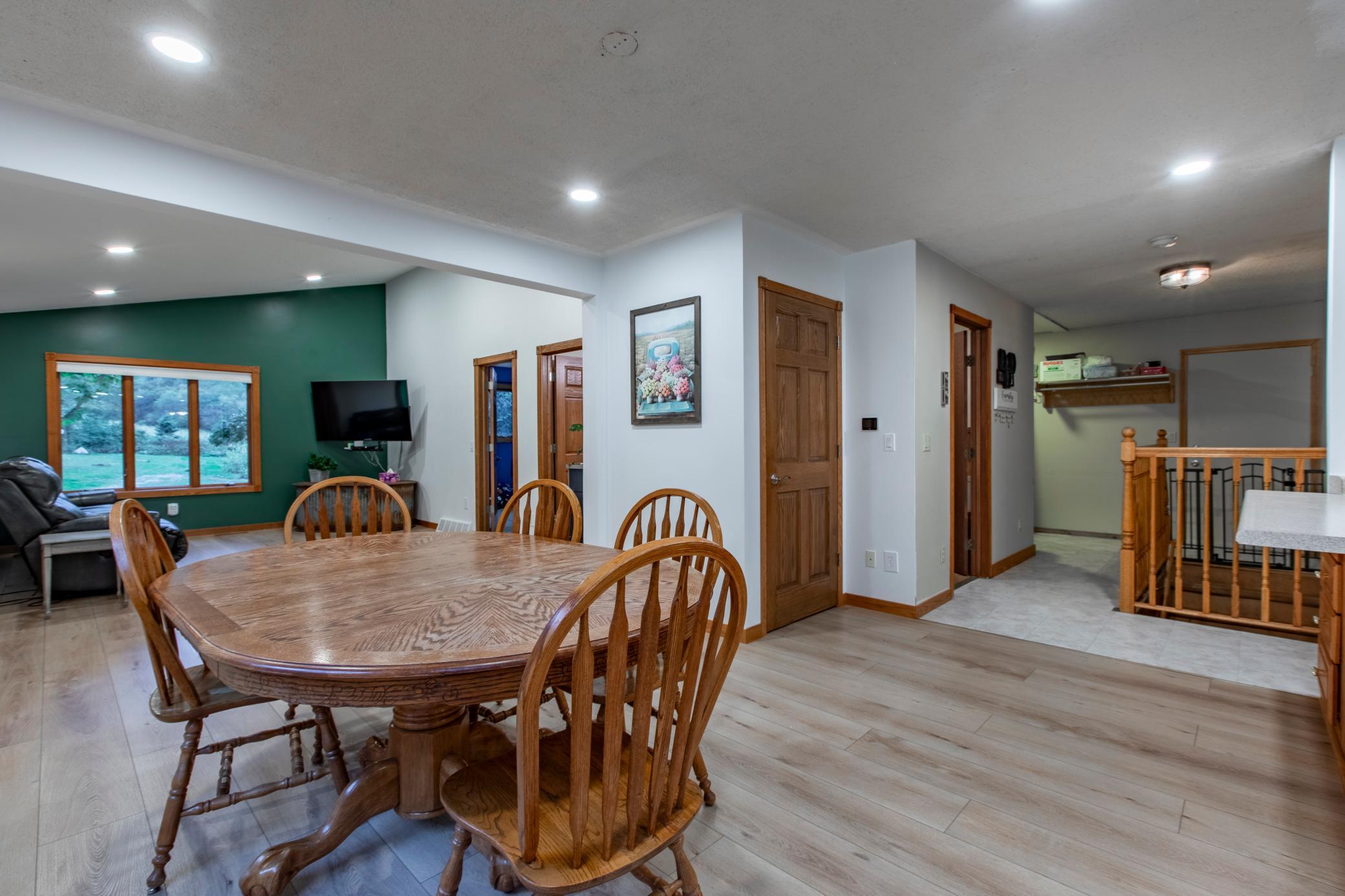 Dining area with a large wooden table, green accent wall, and adjoining hallway and stair landing.
