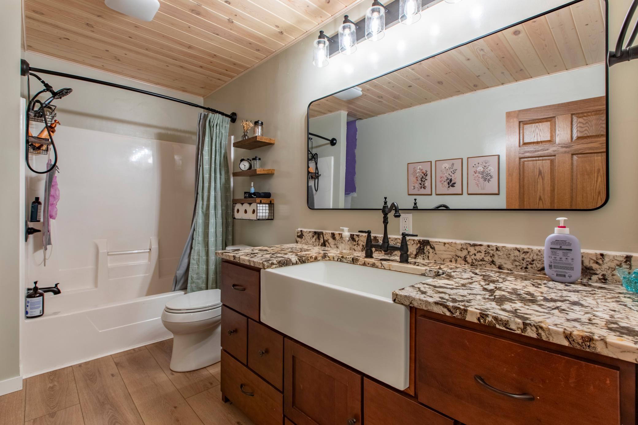 Bathroom with a wood-paneled ceiling, white tub, and dark wood vanity with stone counters.