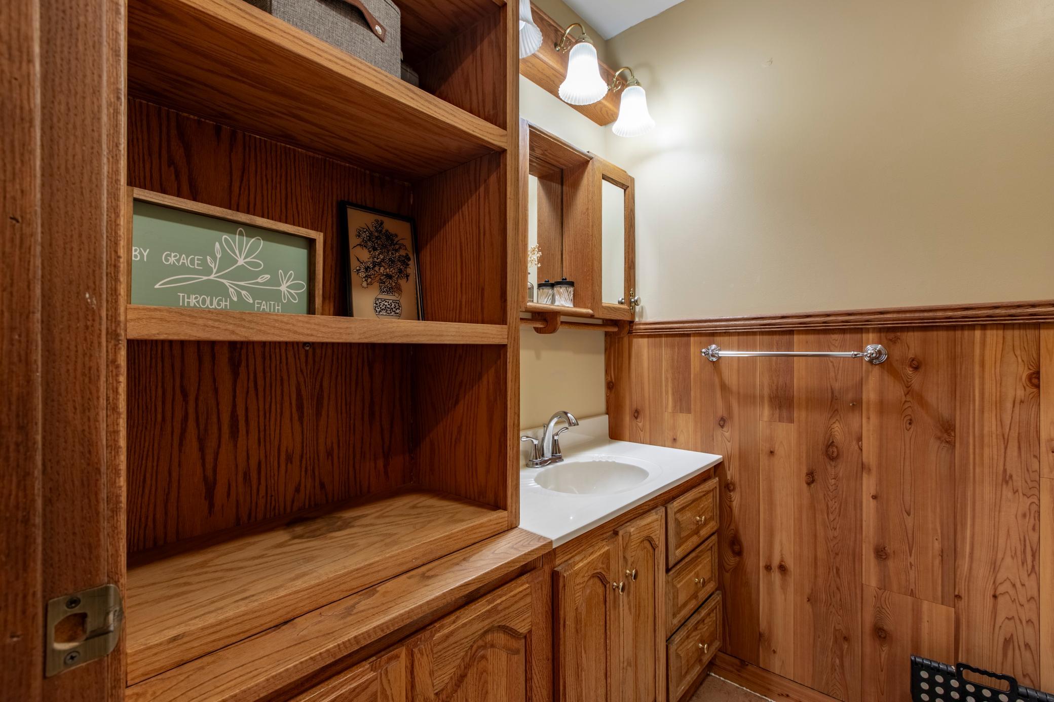 Bathroom vanity and sink beside built-in wooden shelves and wood-paneled walls.